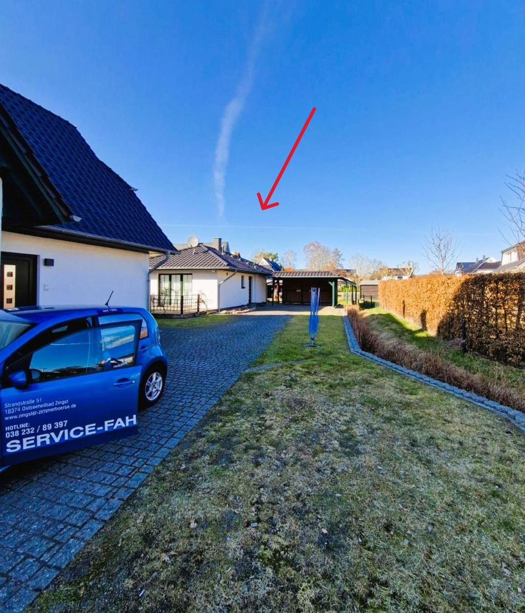 House with paved path, green lawn, and blue car. Sky with cloud.