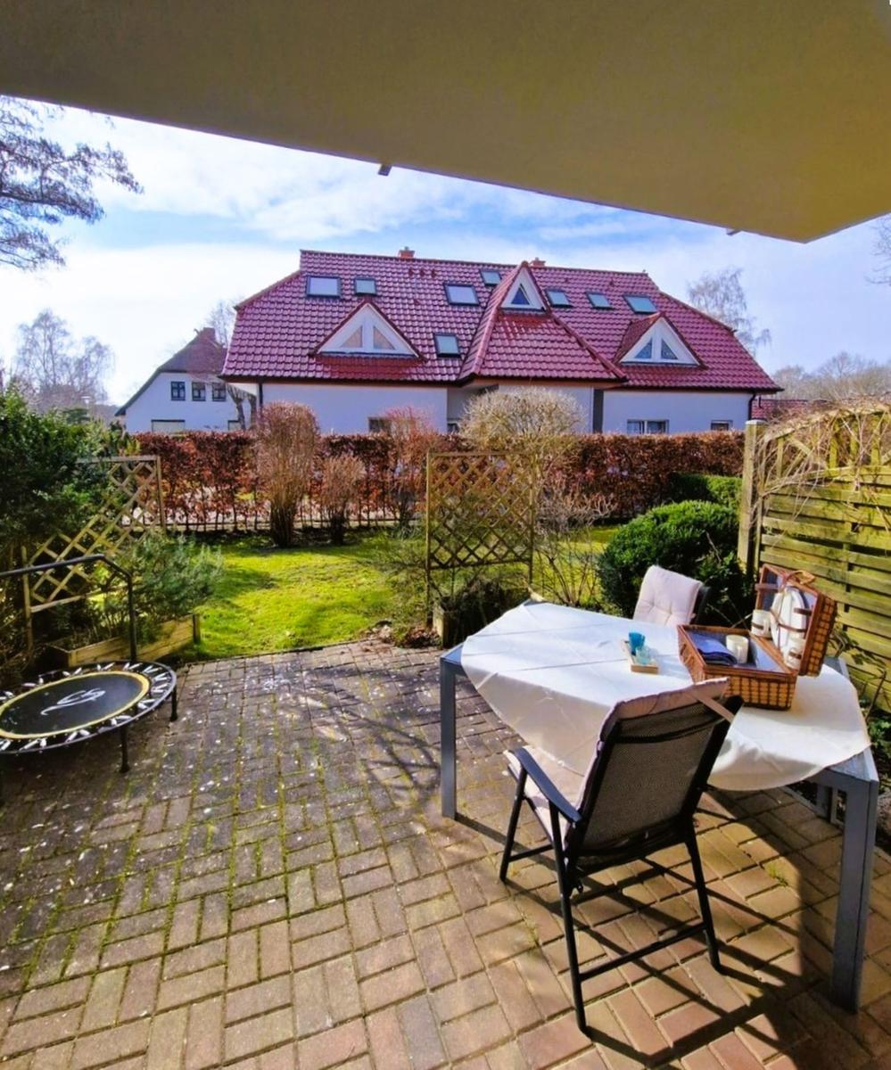 Terrasse mit Tisch, Stühlen und Trampolin. Hinterhof mit Rasen und Zaun. Blick auf ein Haus mit rotem Dach.