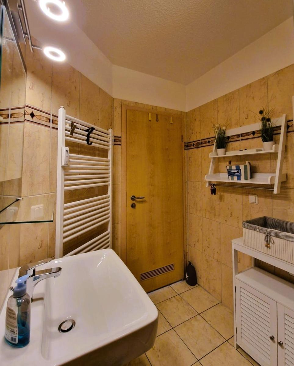Badezimmer mit Waschbecken, Heizkörper, Wandregal und Holztür.