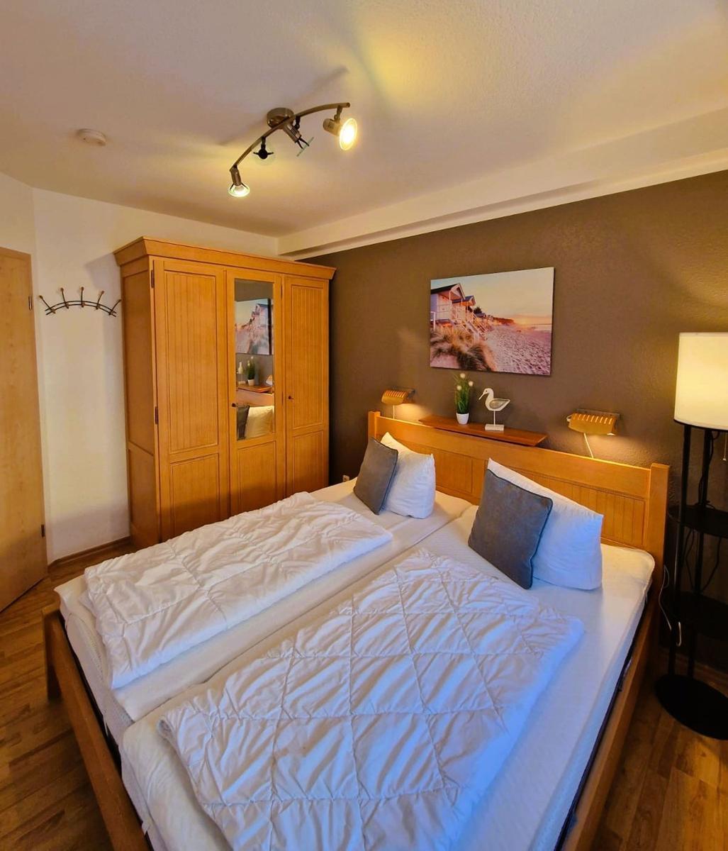 Doppelbett mit weißen Bettwäsche, Holzschrank und Wandbild an der Wand.