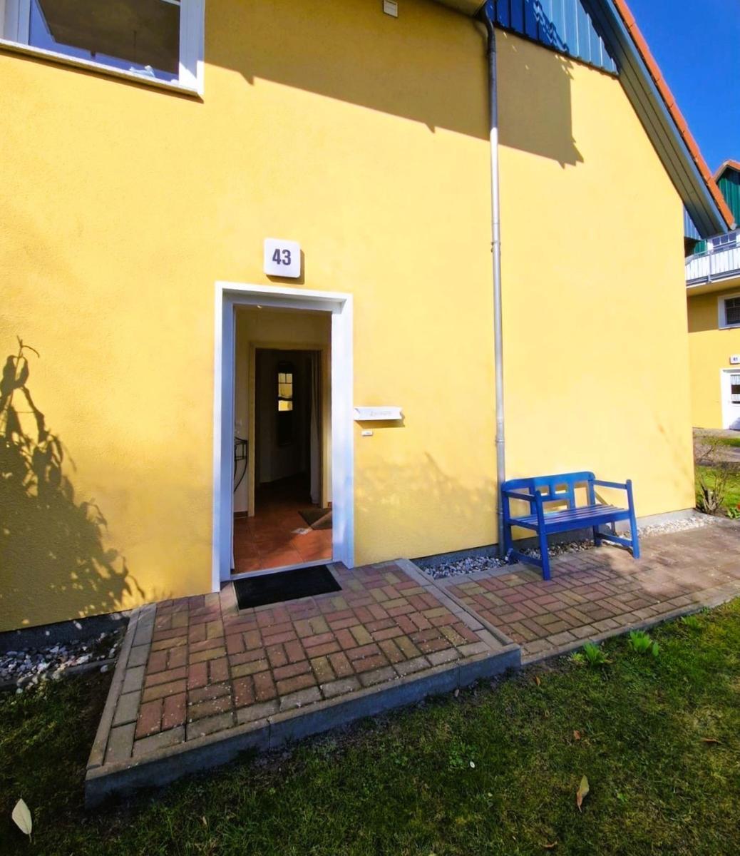Gelbes Haus mit Eingang 43, blauer Bank und gepflastertem Vorgarten.