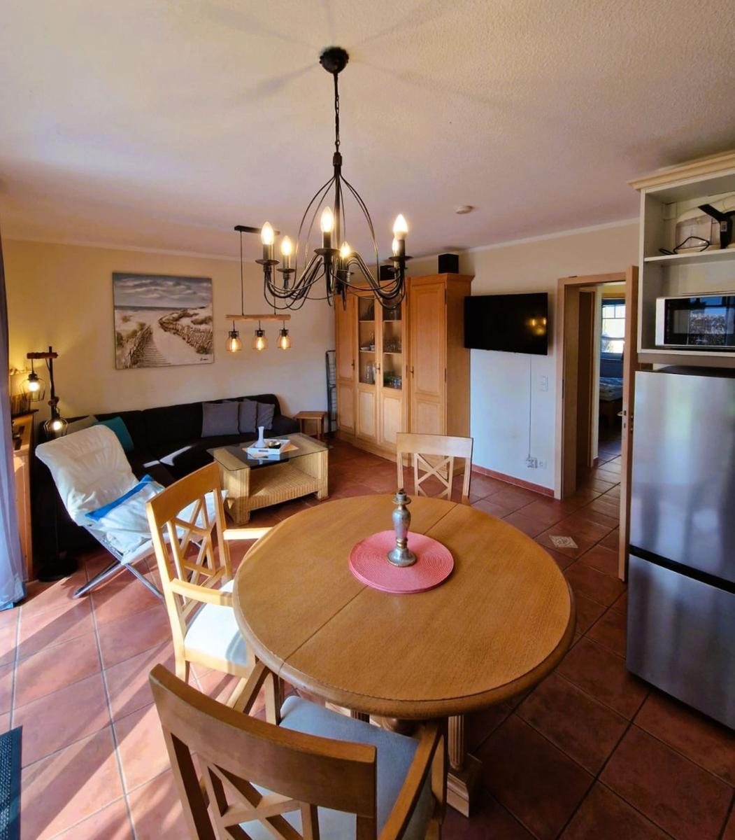 Essbereich mit runden Tisch und Stühlen, Wohnbereich mit Sofa und Fernseher, Küchenbereich mit Kühlschrank.