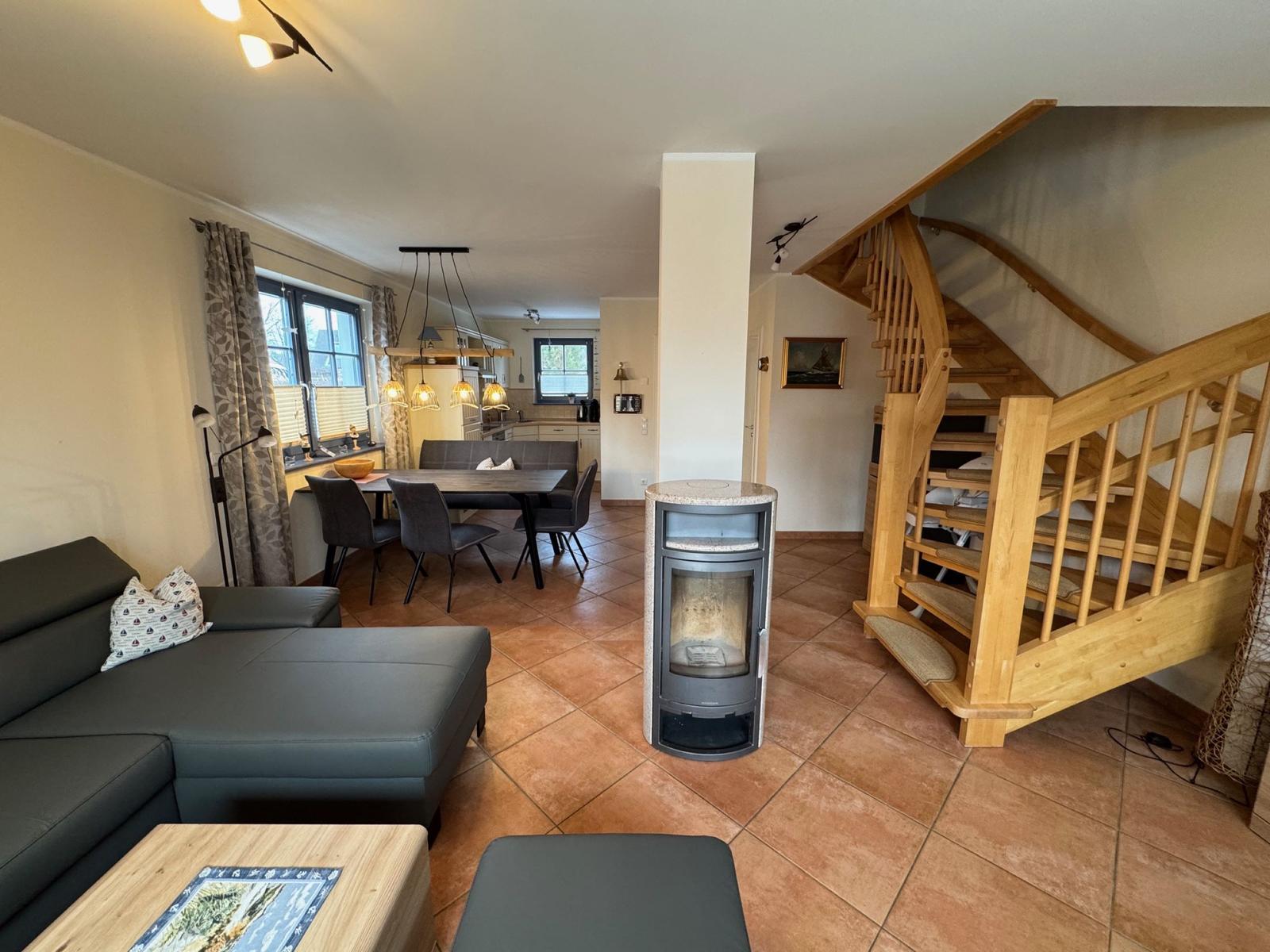 Wohnbereich mit Sofa, Esstisch und Holztreppe. Kaminofen und Terrakottaboden.
