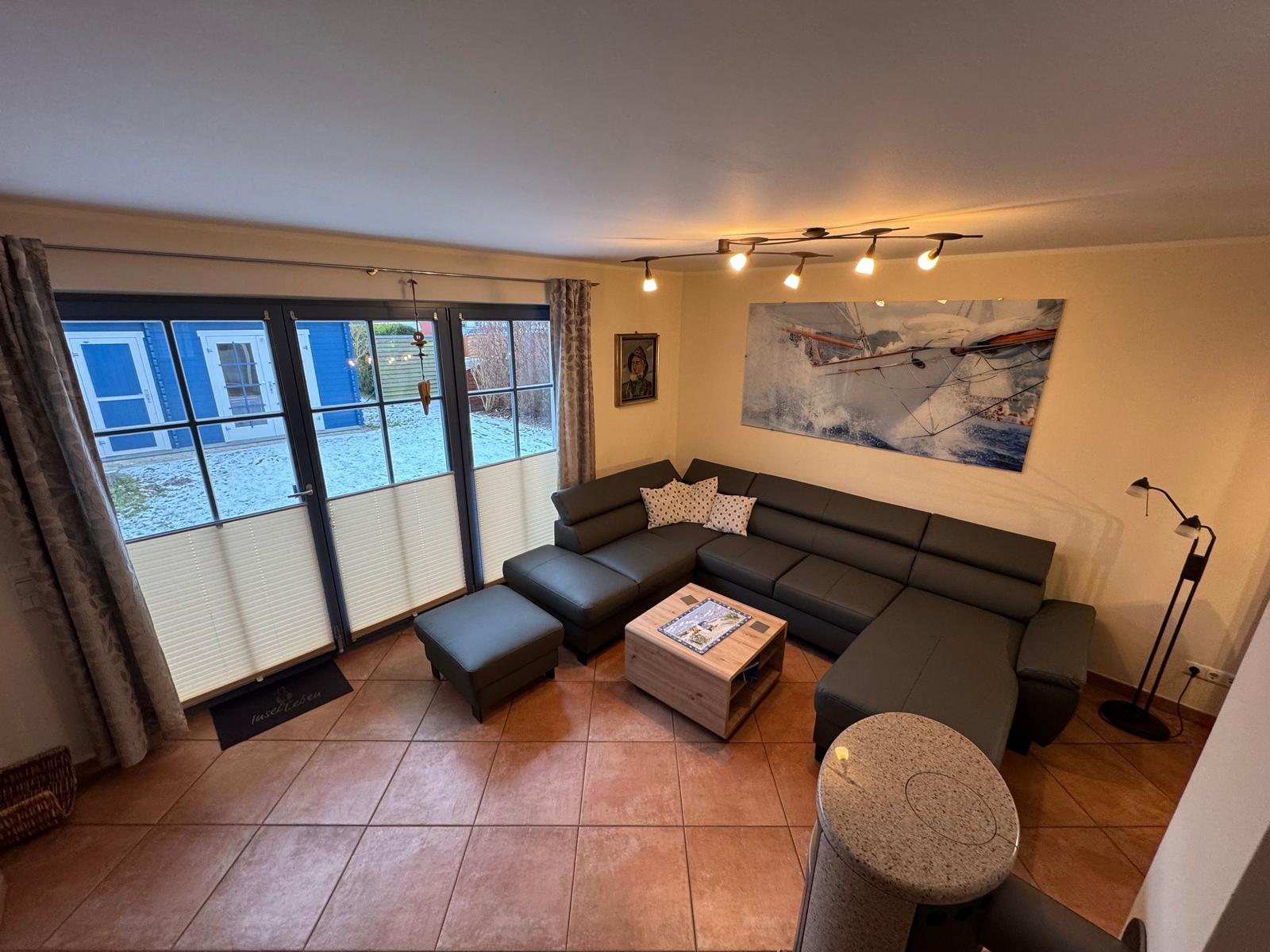 Wohnzimmer mit Ecksofa, Holztisch und Fenster zur Außenterrasse.