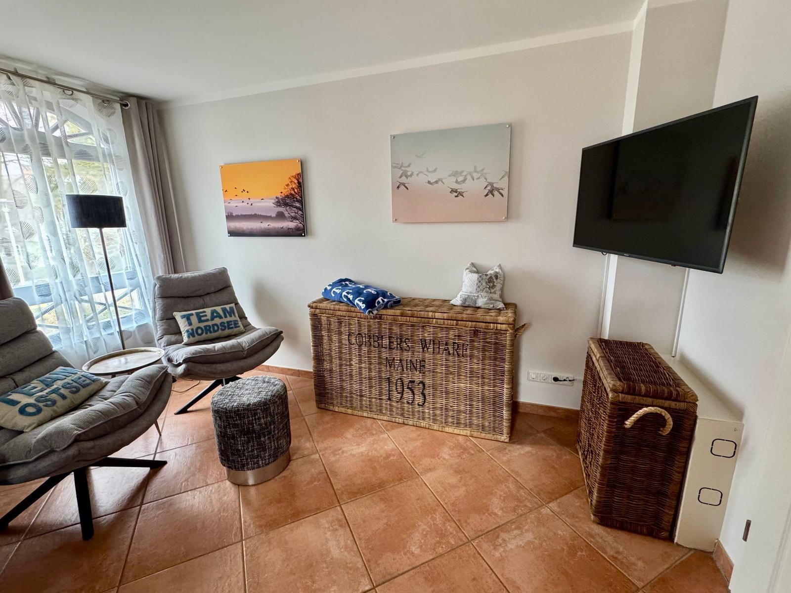 Wohnzimmer mit zwei Sesseln, Fernseher und Korbboxen an der Wand.