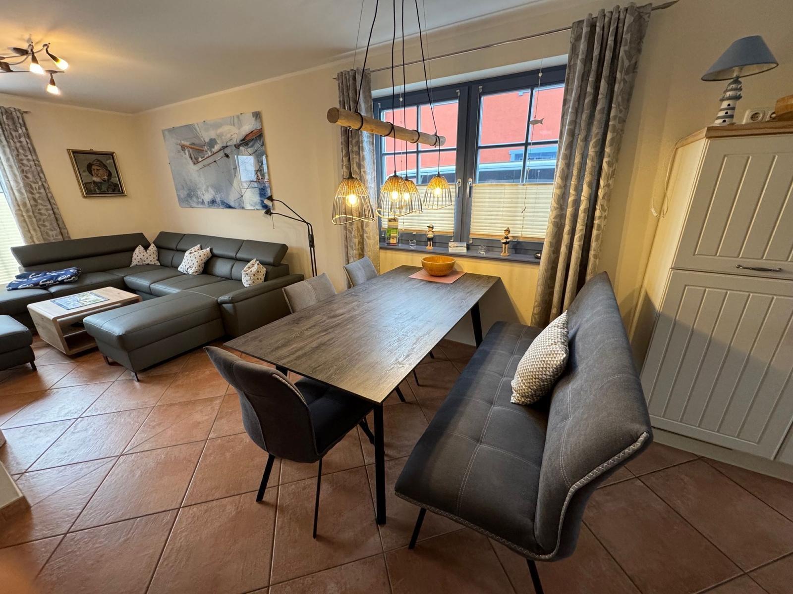 Esszimmer mit Tisch, Stühlen und Sofa. Fenster mit Vorhängen. Hängelampe und Wandbild.