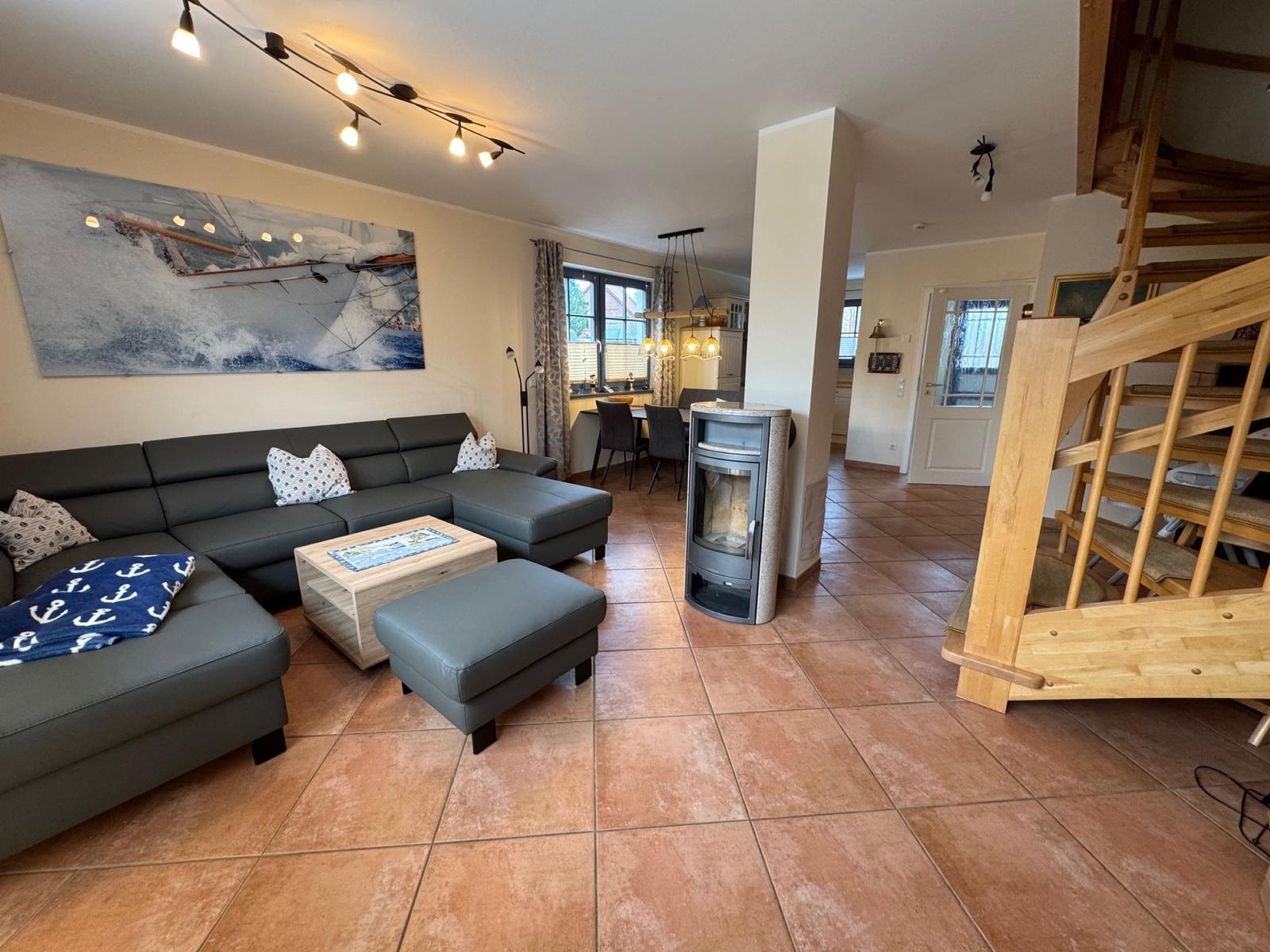 Wohnzimmer mit Sofa, Kamin und Holztreppe. Wandbild zeigt Segelyacht.