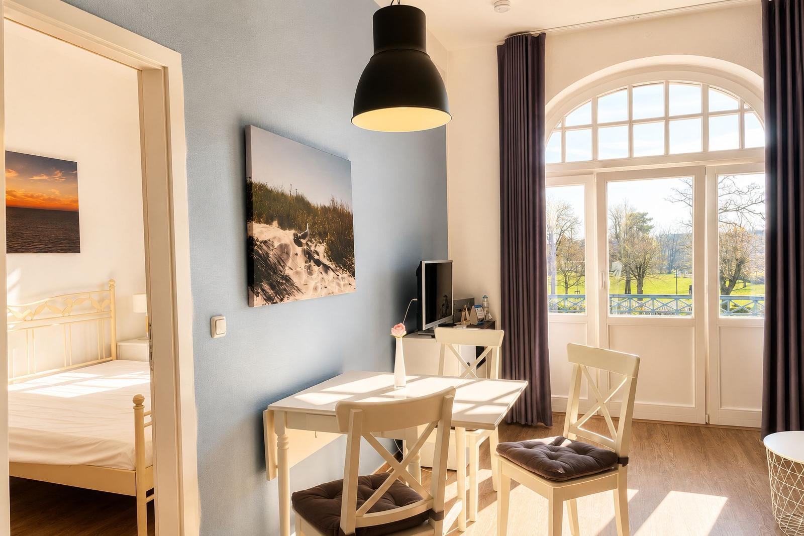 Wohnbereich mit Tisch, Stühlen und Blick auf grüne Landschaft durch Fenster.