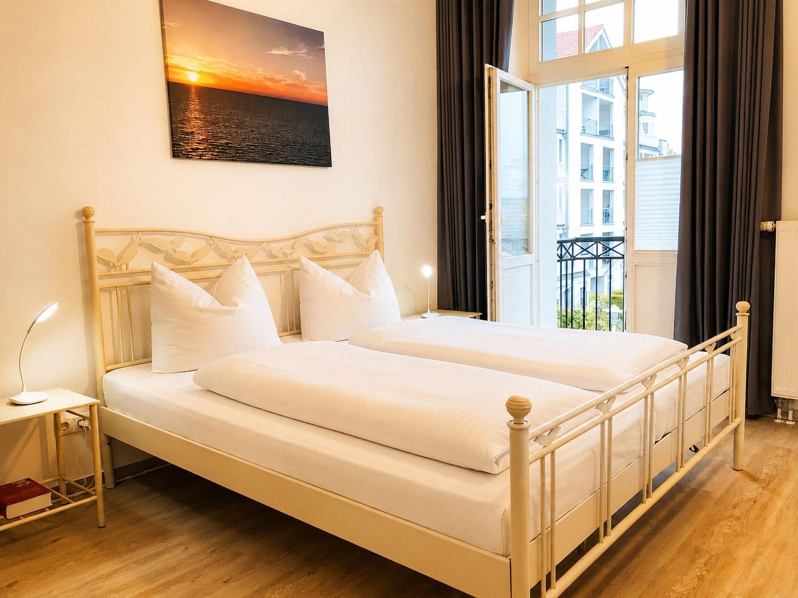 Ein Schlafzimmer mit einem Bett, einem Bild an der Wand und einer Tür zum Balkon.