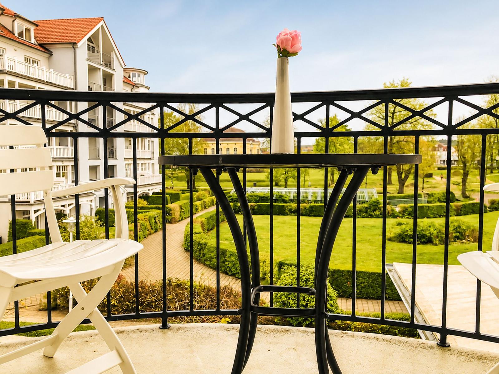 Terrasse mit Tisch, Stühlen und Blume. Blick auf gepflegten Garten und Gebäude.