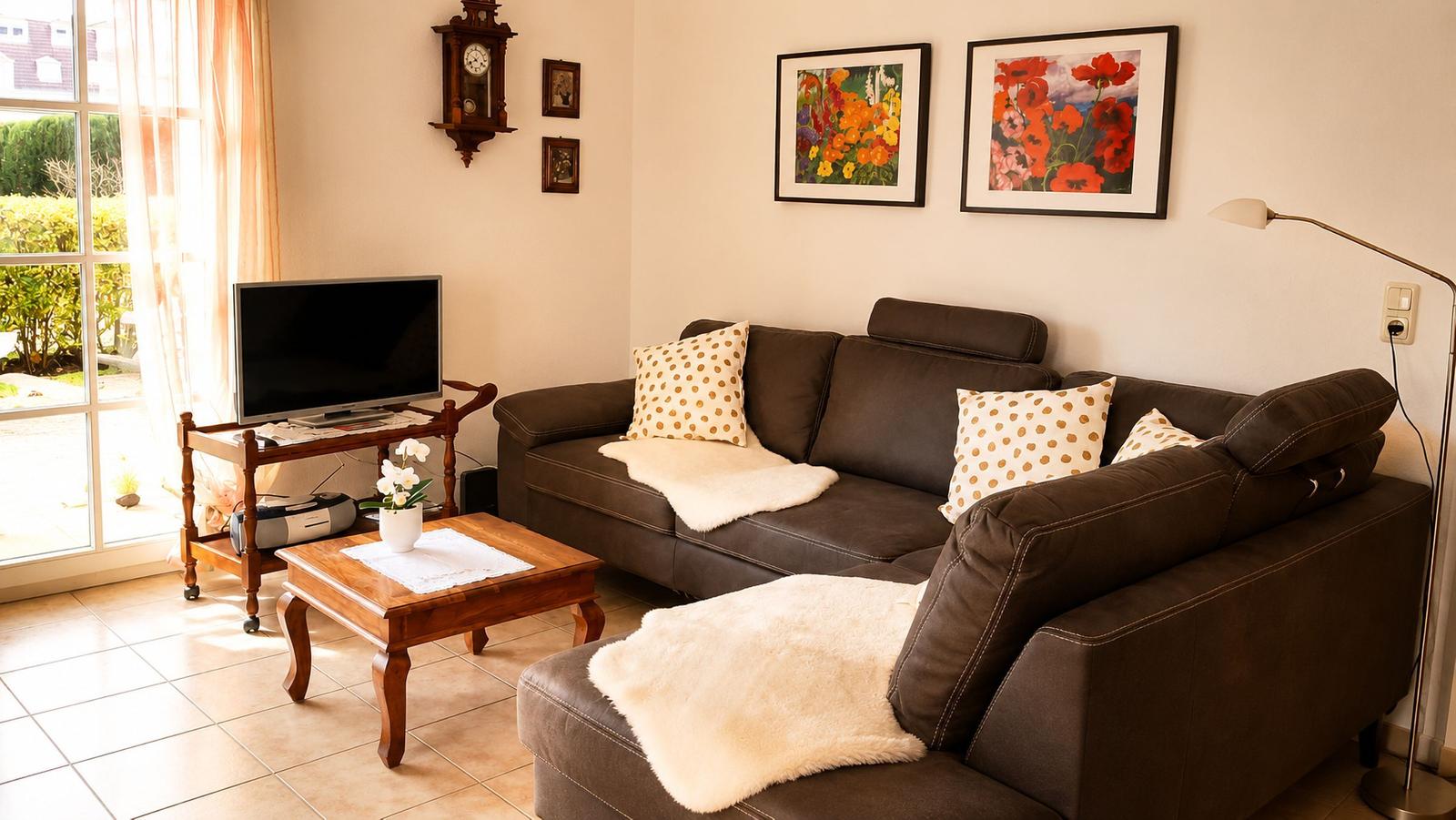 Ein Wohnzimmer mit braunem Sofa, Holztisch und Fernseher. An der Wand hängen zwei Bilder.