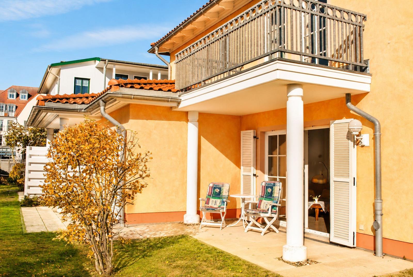 Terrasse mit zwei Stühlen und Tisch. Balkon mit Geländer. Gelber Hauswänden und grüner Rasen.