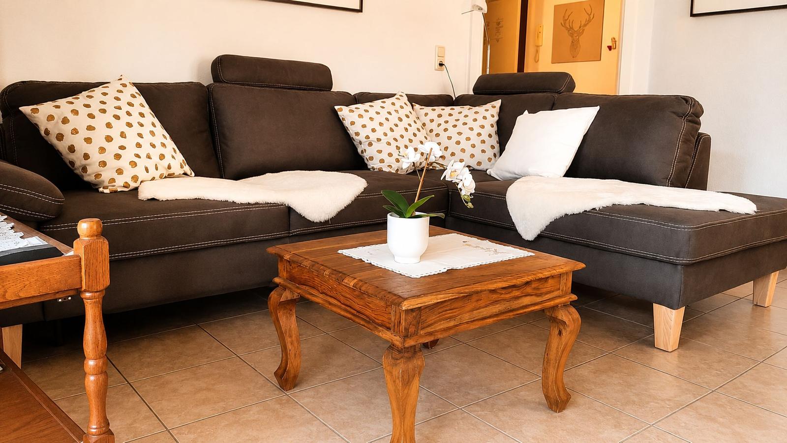 Ein Wohnzimmer mit braunem Sofa, Kissen und einem Holztisch mit Pflanze.