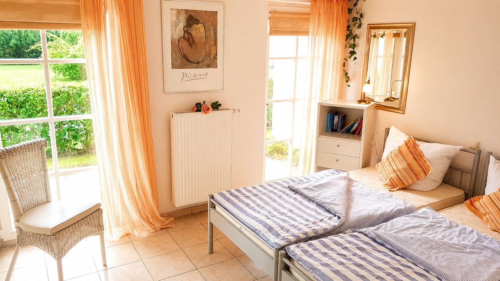 Zwei Betten mit Streifenbettenlaken, Fenster mit orangefarbenen Vorhängen und Wandbild.