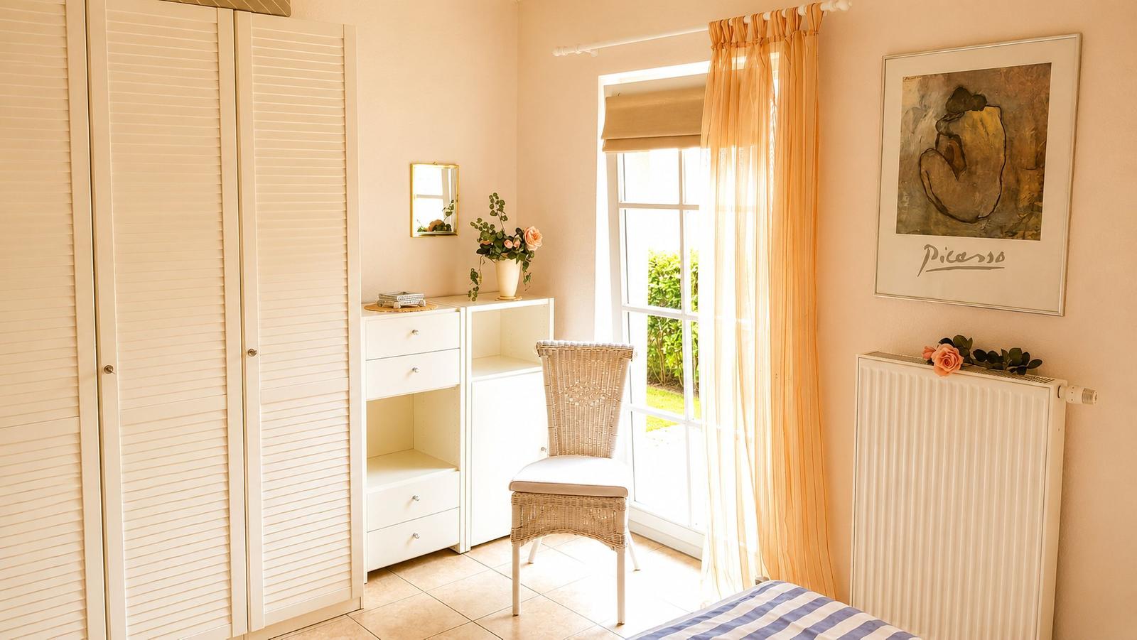 Schlafzimmer mit Kleiderschrank, Schreibtisch, Stuhl und Fenster mit Gardinen.
