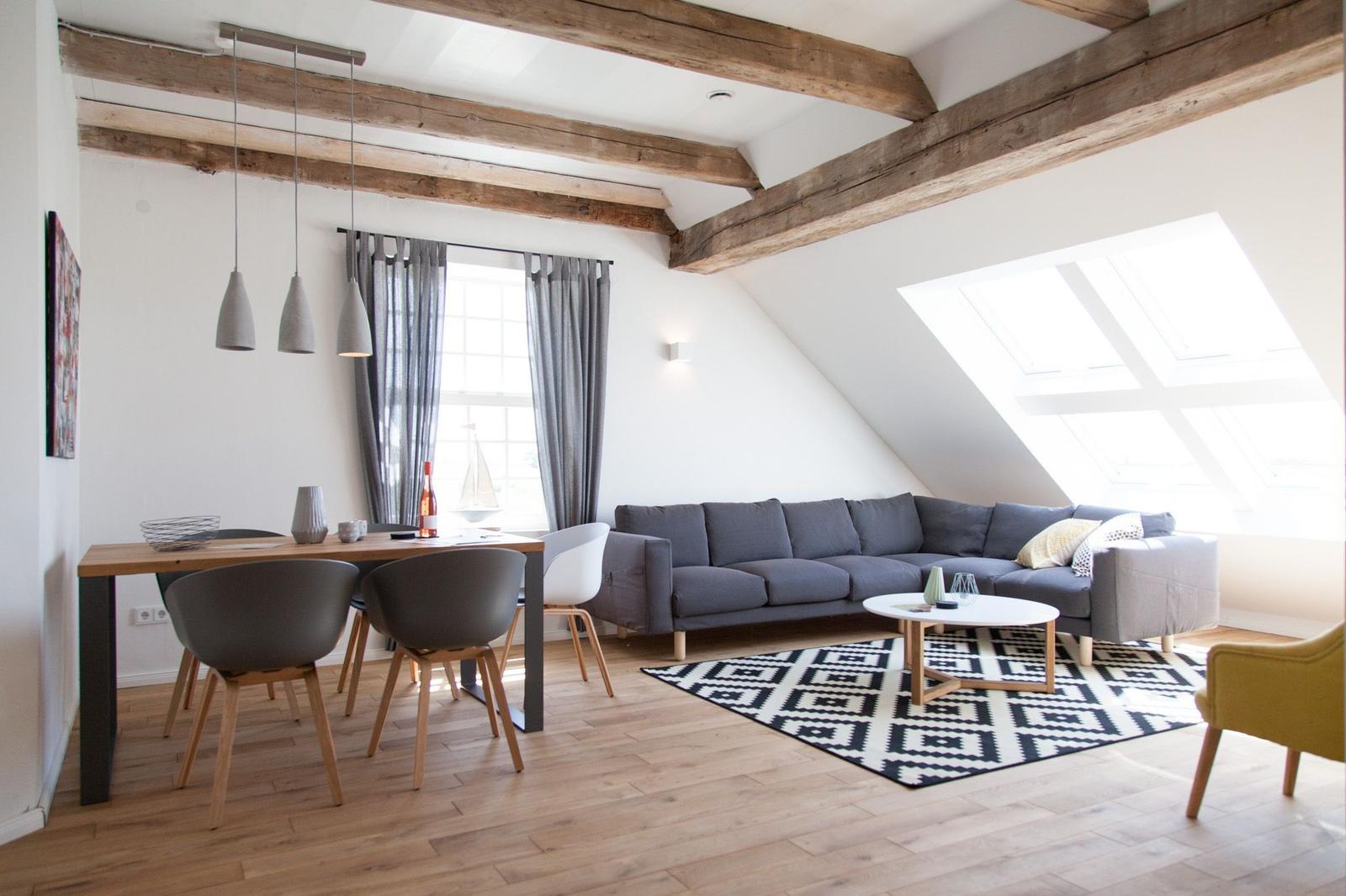 Wohn- und Essbereich mit Holzbalken, Sofa, Tisch und Sitzgelegenheiten.