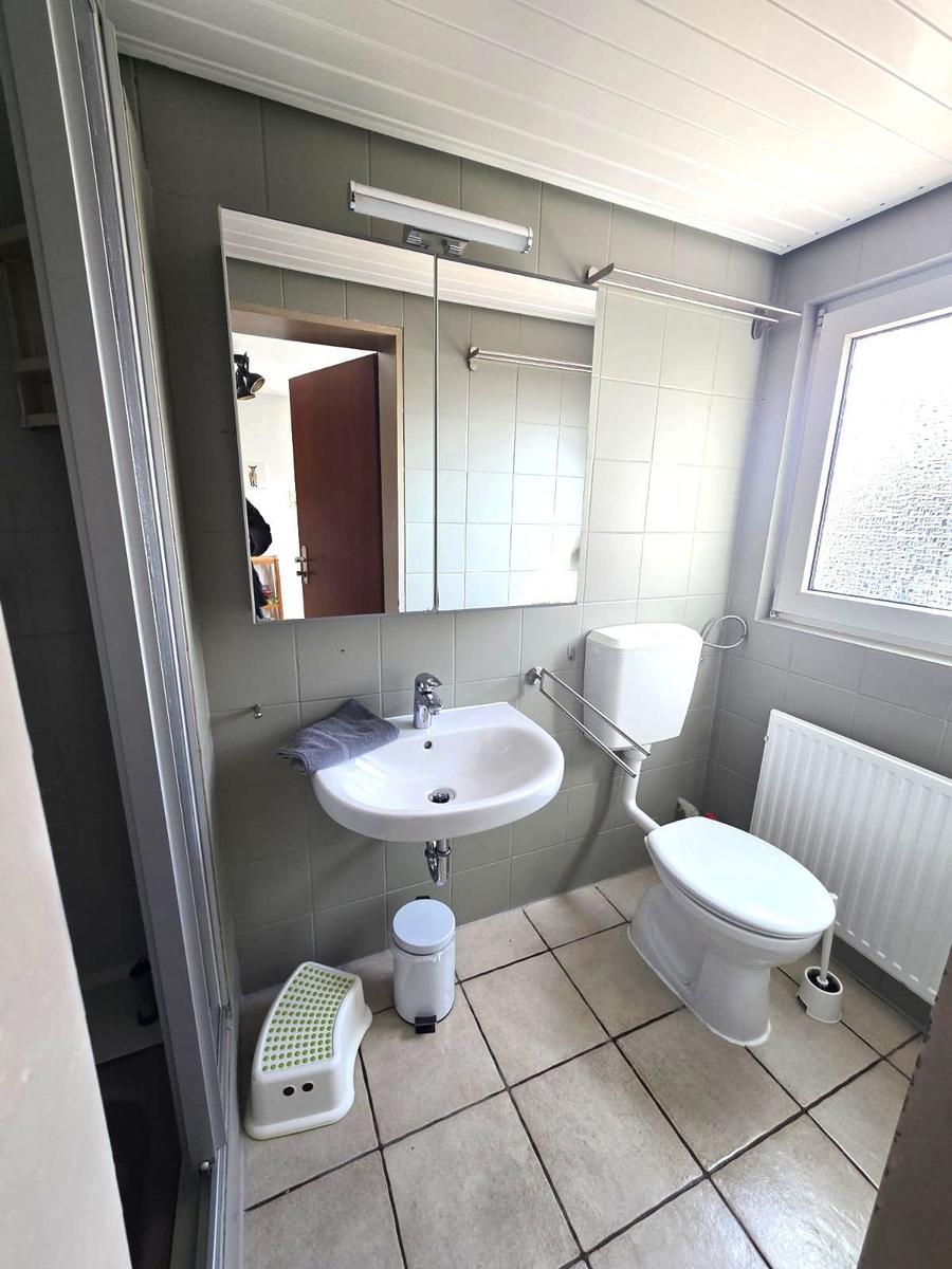 Bathroom with sink, toilet, and mirror. Window and radiator are present.