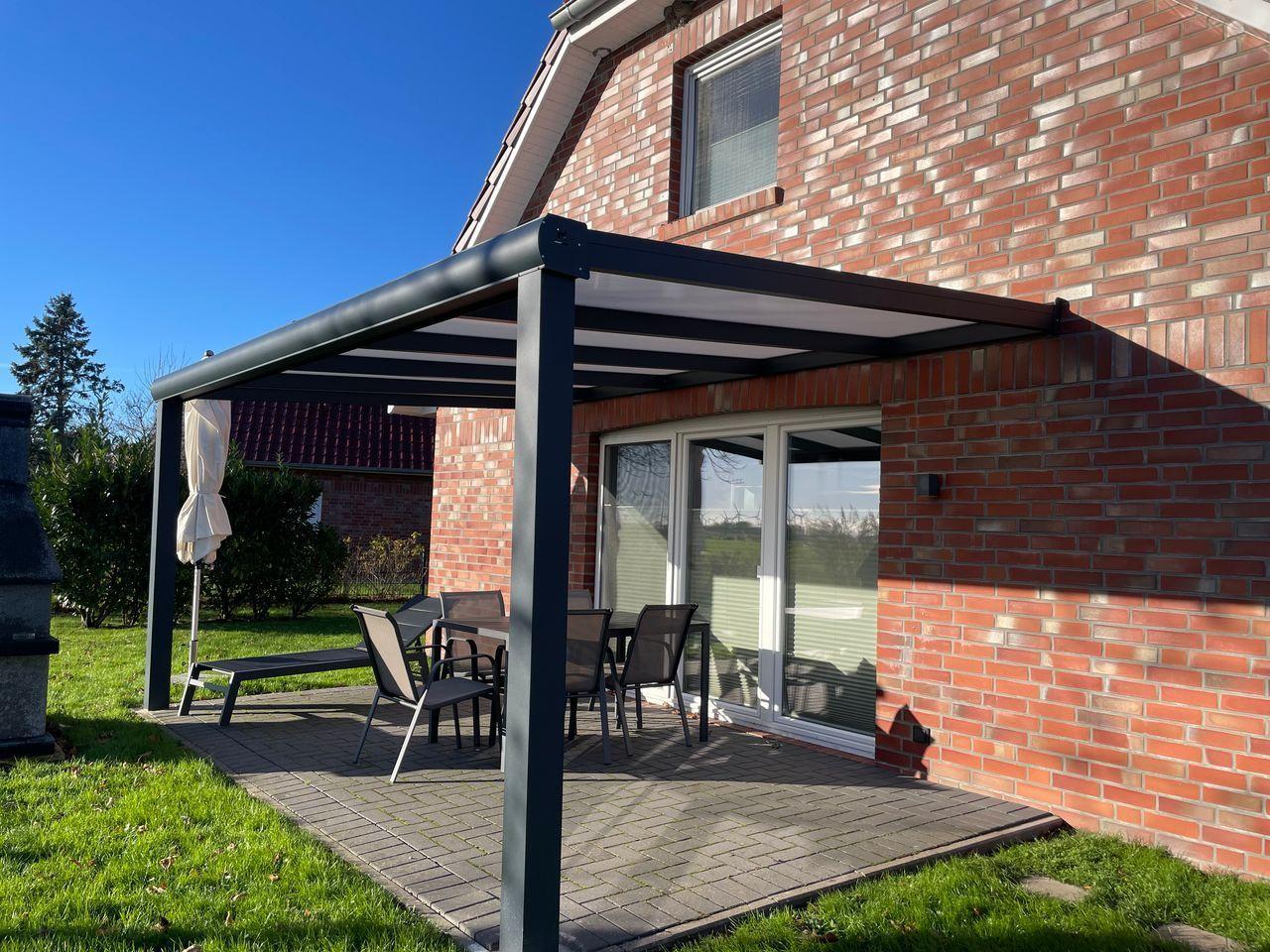Terrasse mit Sonnenschutz, Tisch, Stühlen und Liege unter einem Pavillon neben einem Haus.