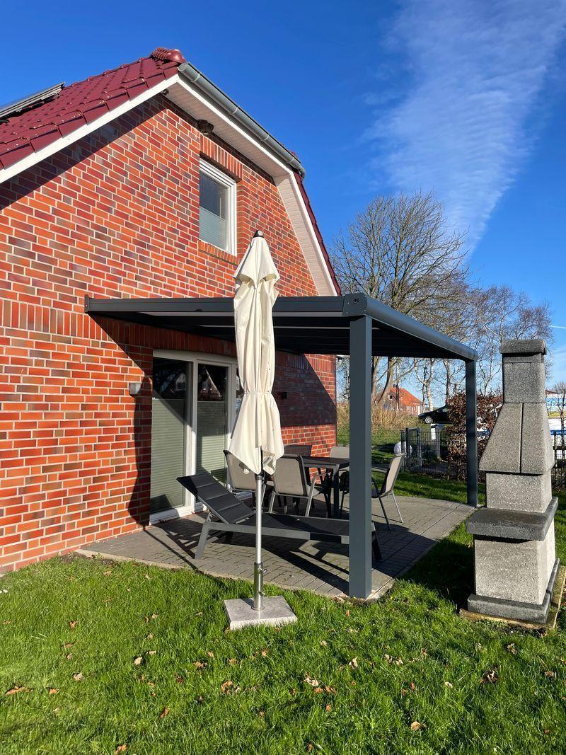 Rotes Backsteinhaus mit Terrasse, Sonnenschutz und Grillplatz im Garten.