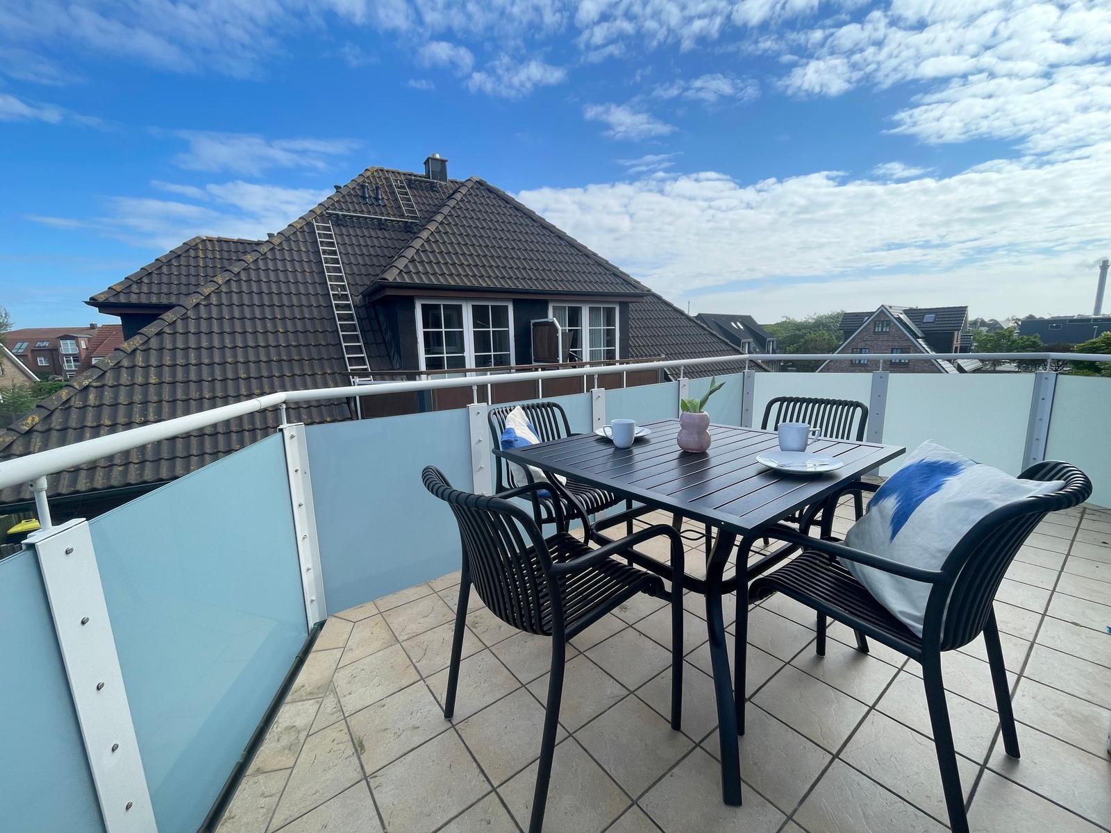 Terrasse mit Tisch und Stühlen, Blick auf Dächer und Himmel.