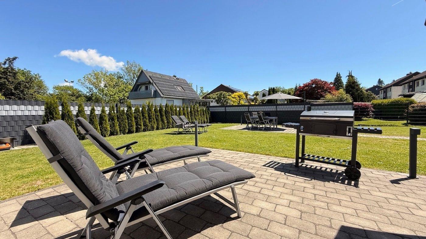 Hinterhof mit Liegestühlen, Grill und Gartenbereich. Blick auf benachbarte Häuser.