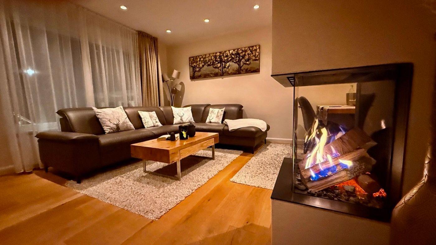 Ein Wohnzimmer mit Ledersofa, Holzfußboden und Kaminofen mit brennenden Holzscheiten.