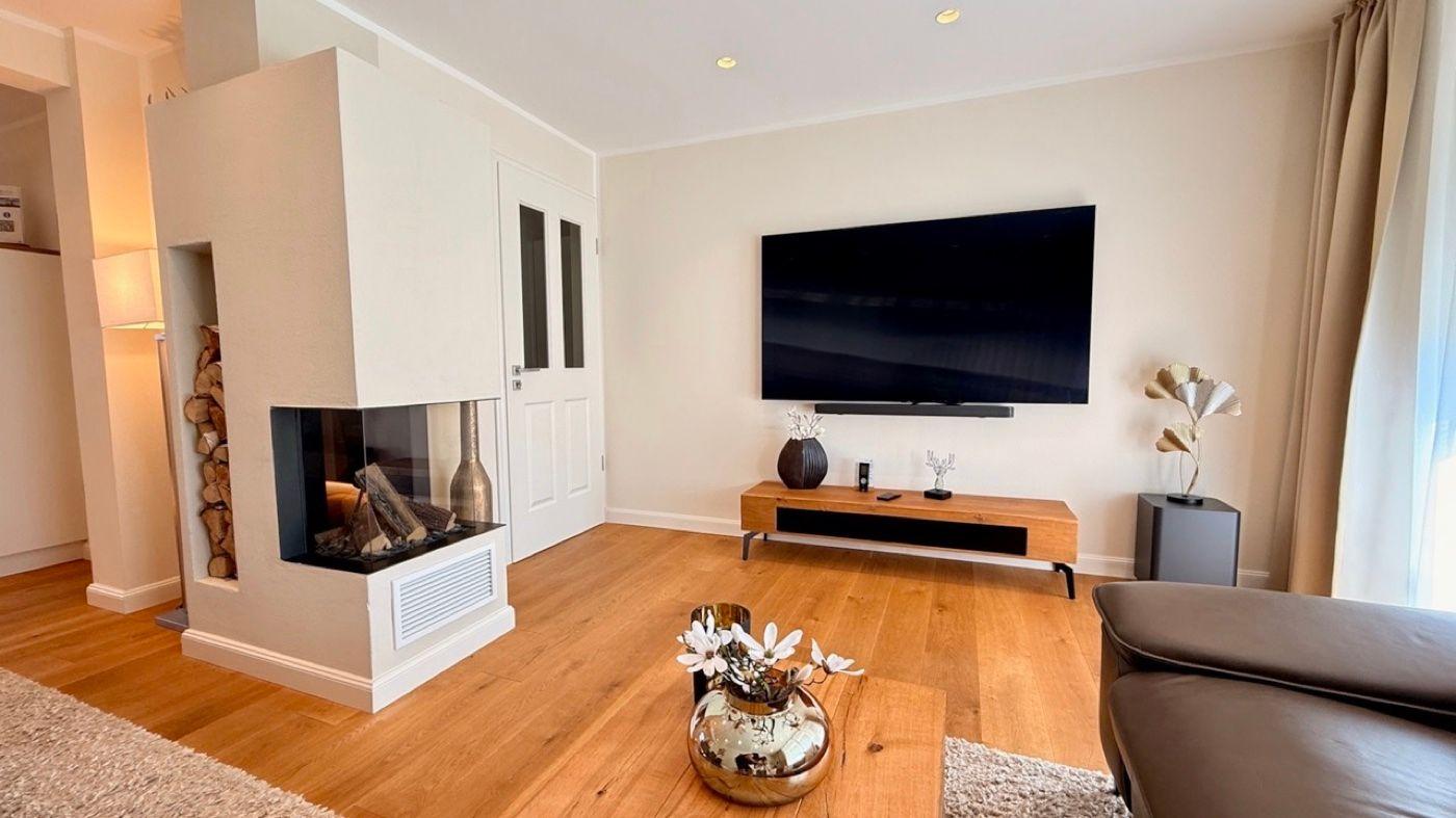 Wohnzimmer mit Kamin, Fernseher und Holzboden.