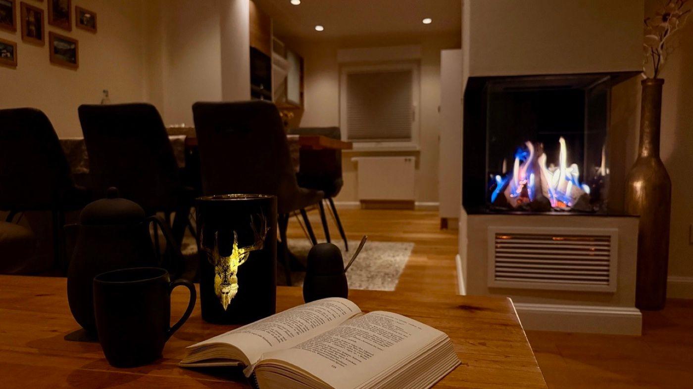 Ein Tisch mit Buch, Tassen und einem Kamin im Hintergrund.