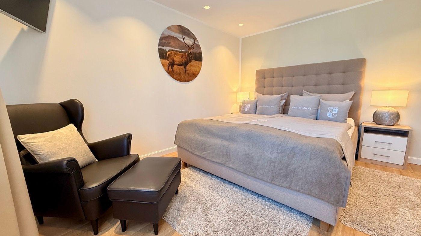 Schlafzimmer mit Bett, Sessel und Wandbild eines Hirsches.