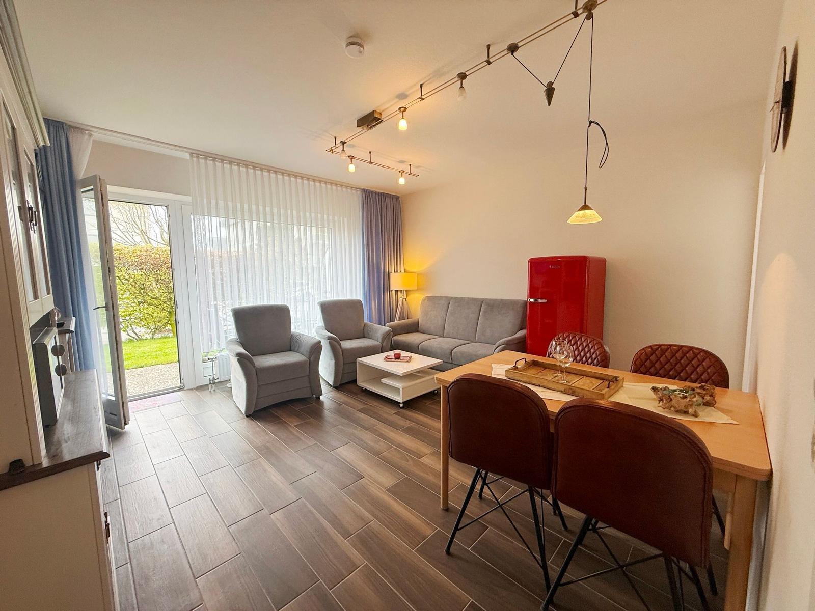 Wohn- und Essbereich mit Sofa, Stühlen und rotem Kühlschrank.