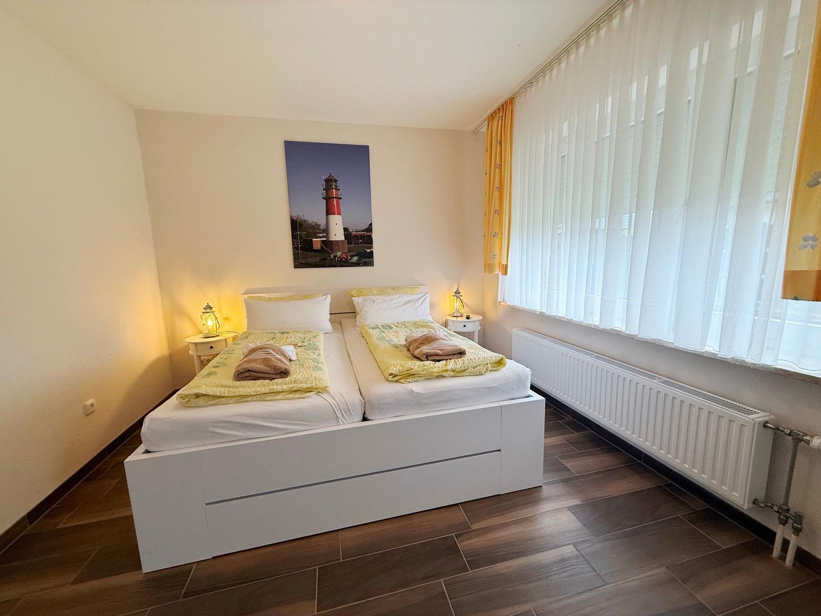 Schlafzimmer mit Doppelbett, Fenster mit Jalousien und Wandbild eines Leuchtturms.