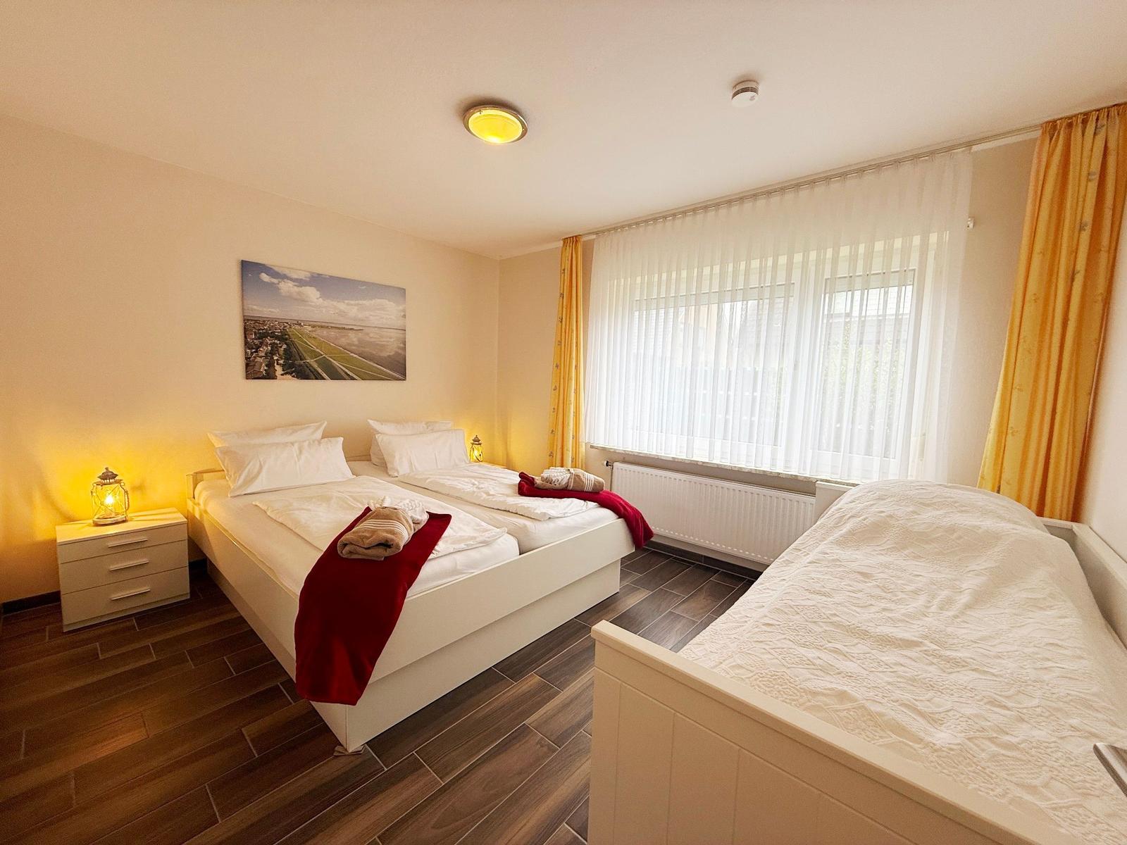 Zimmer mit zwei Betten, Fenster mit Vorhängen und Wandbild.