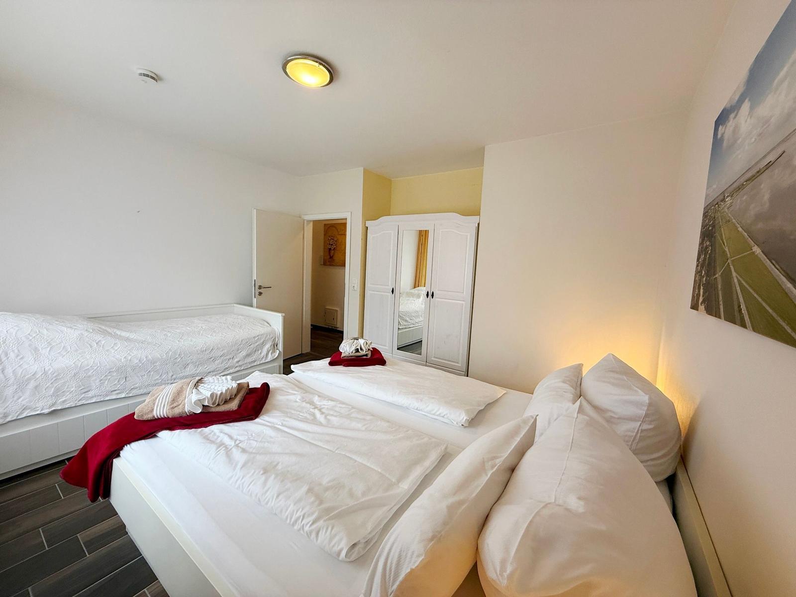 Zwei Betten mit weißen Laken, Schrank und Wandbild in einem Schlafzimmer.