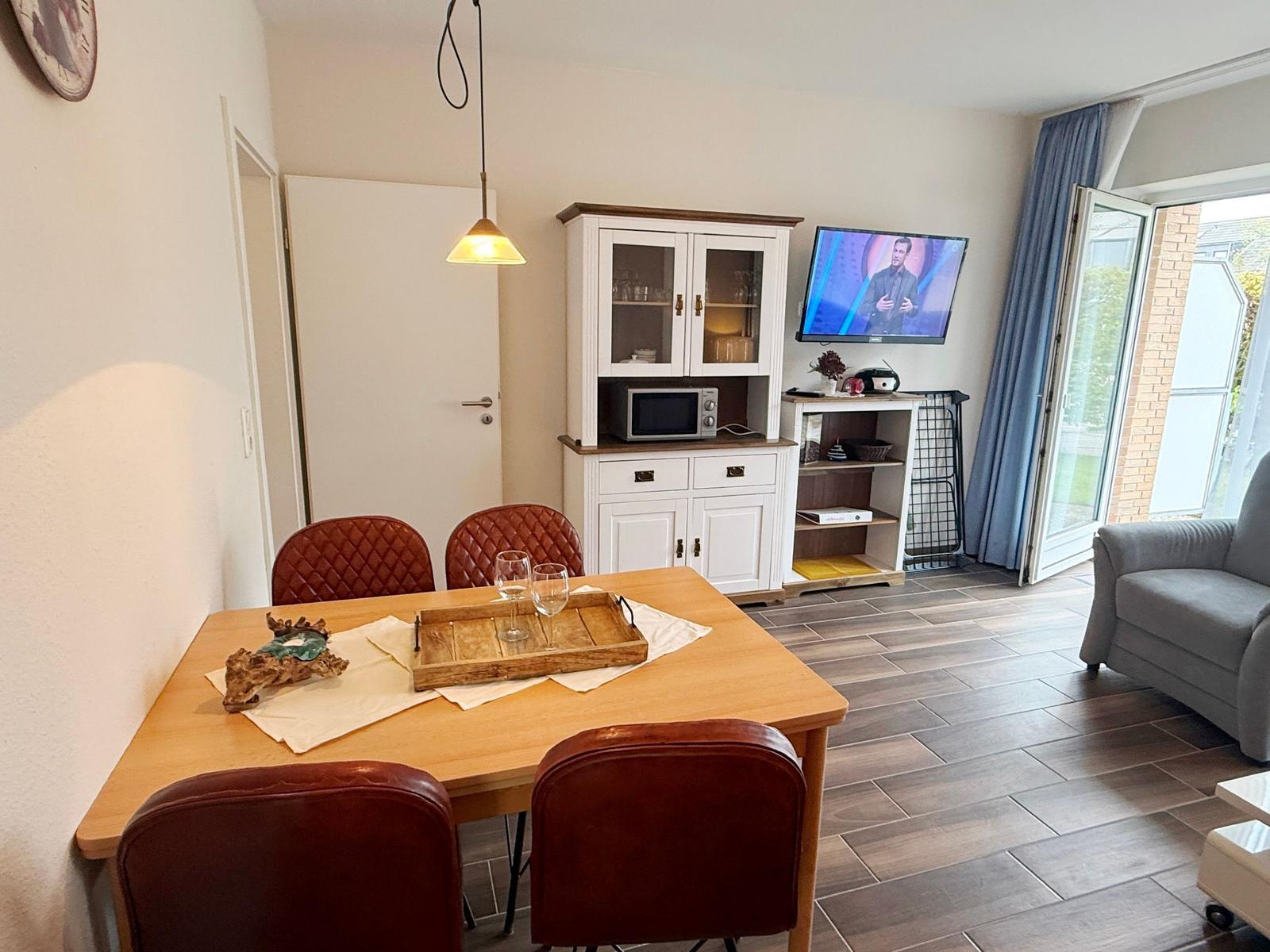 Esszimmer mit Tisch, Stühlen und Fernseher. Durchgang zur Terrasse mit Sitzgelegenheit.