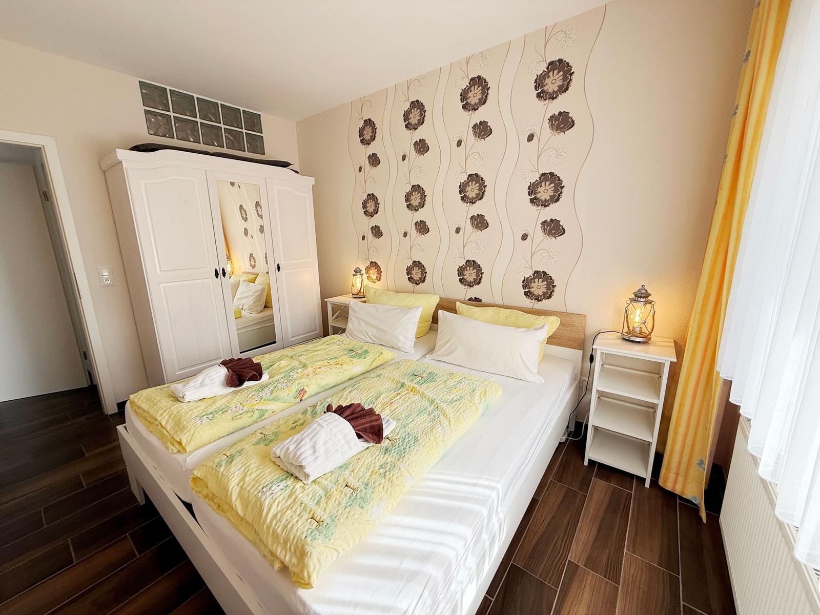 Schlafzimmer mit Doppelbett, Kleiderschrank und Blumenaufdruck an der Wand.