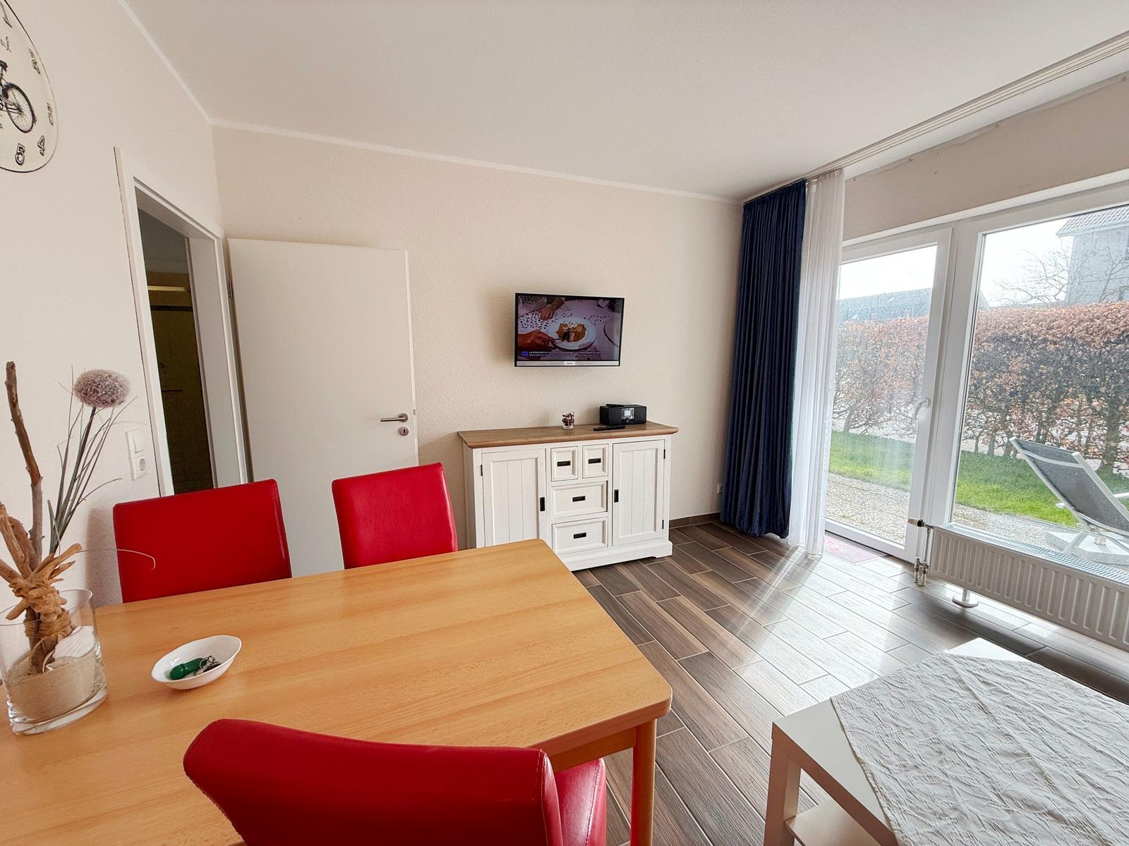 Essbereich mit roten Stühlen und TV. Terrasse mit Liege. Blick auf Garten.