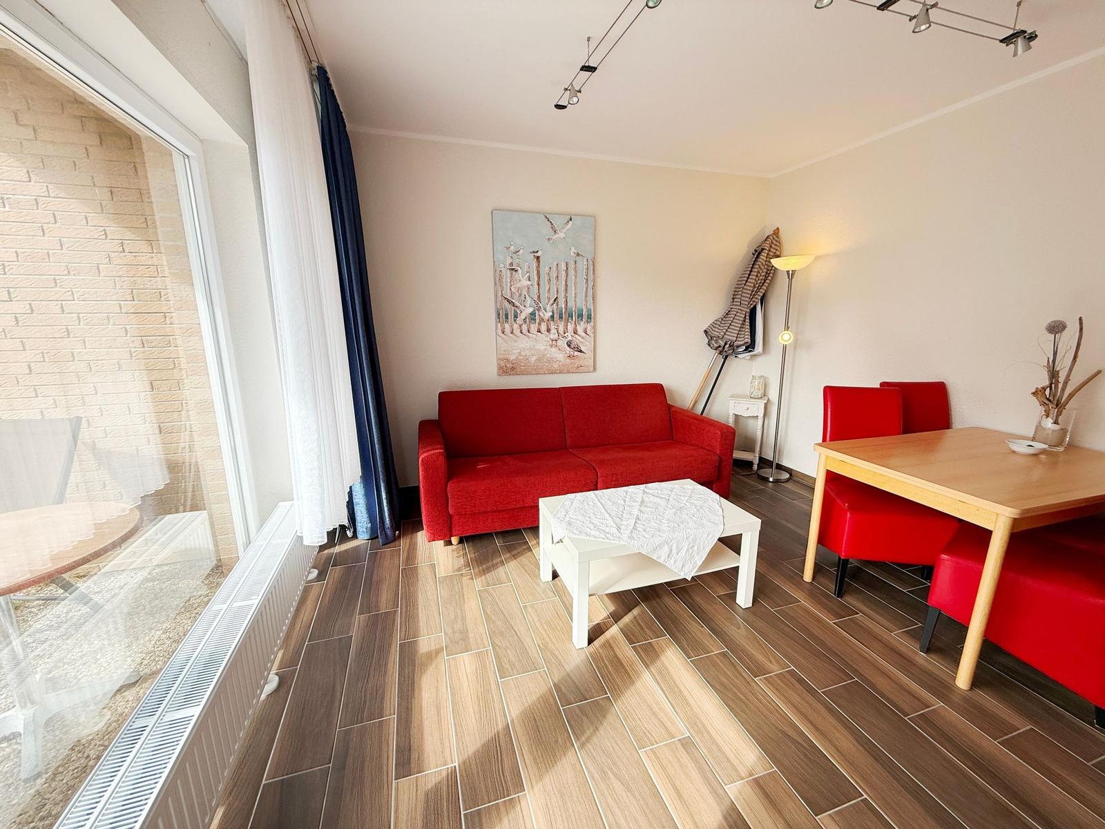 Wohnzimmer mit rotem Sofa, Esstisch und Holzboden. Große Glasfront mit Blick auf Terrasse.
