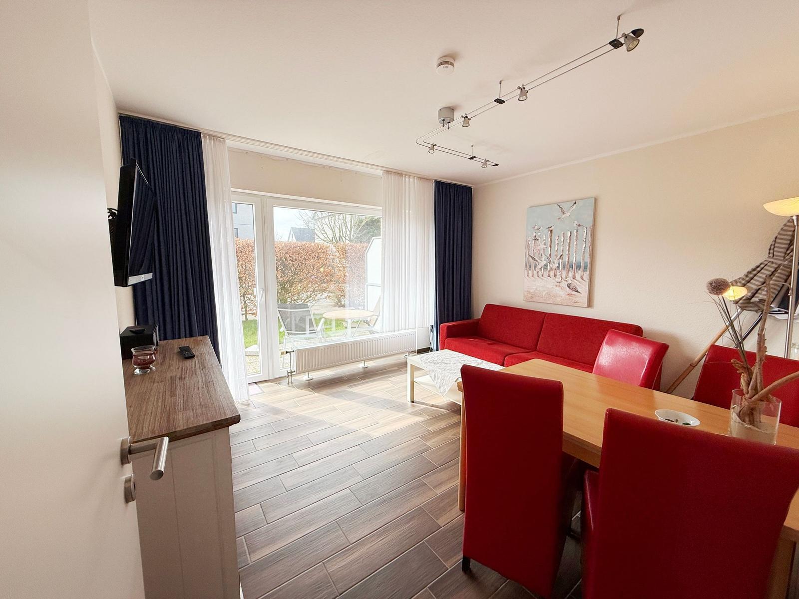 Wohn- und Essbereich mit rotem Sofa und Stühlen, Fernseher und Terrasse.