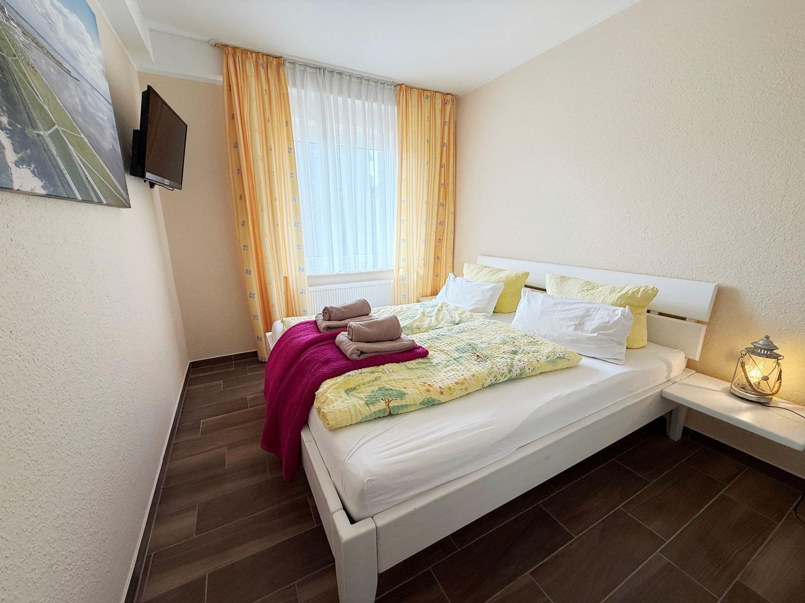 Schlafzimmer mit Bett, Fenster, TV und Nachttisch.