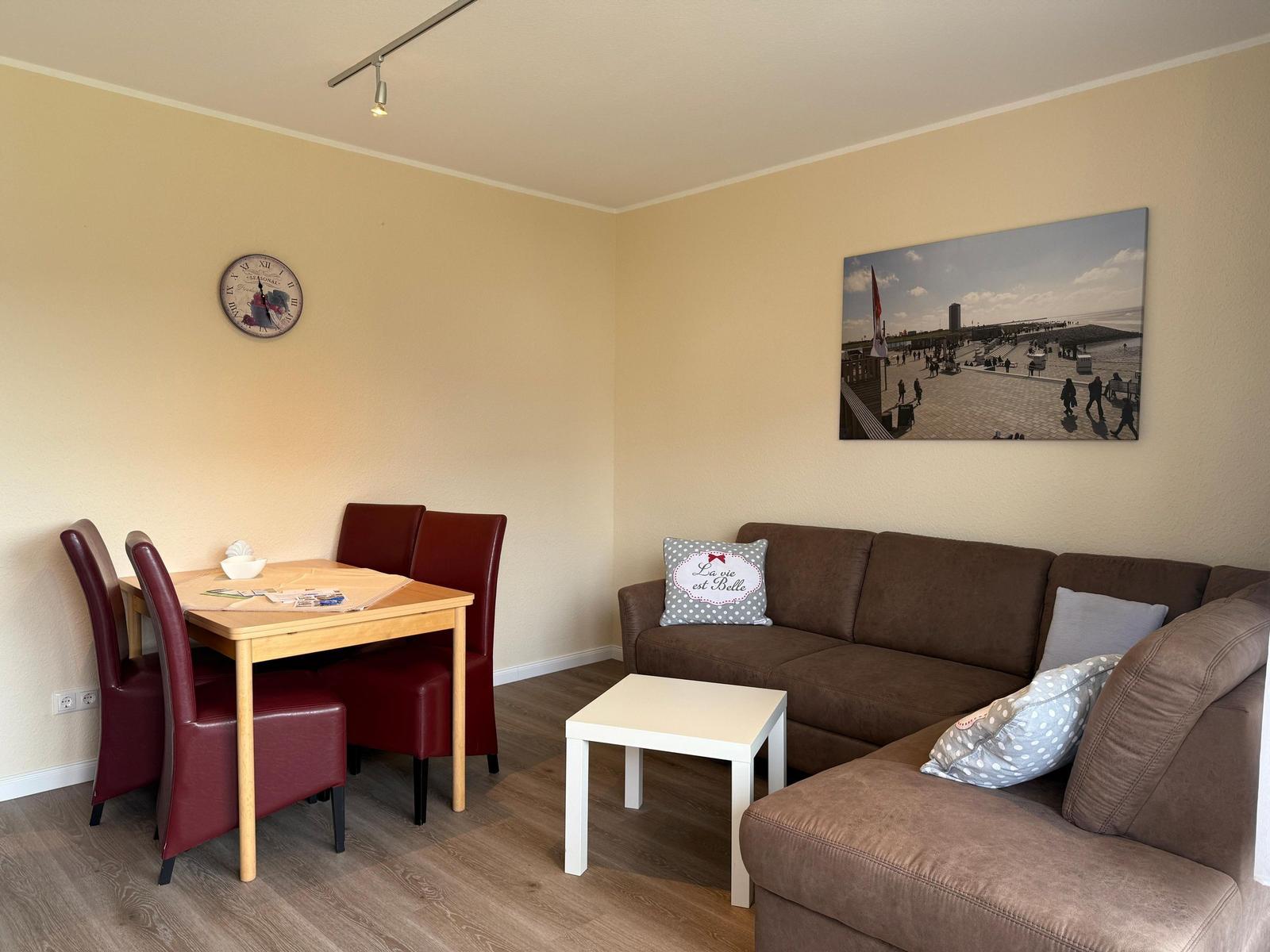 Wohn- und Essbereich mit Sofa, Tisch und Stühlen sowie Wandbild und Uhr.