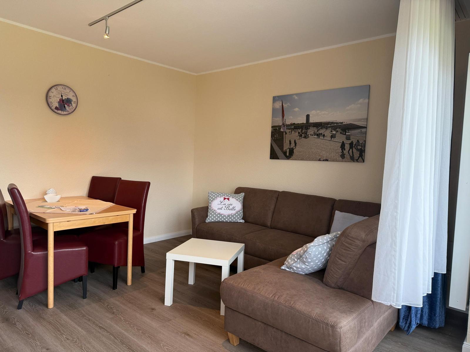 Wohn- und Essbereich mit Sofa, Tisch und Stühlen sowie Wandbild und Uhr.