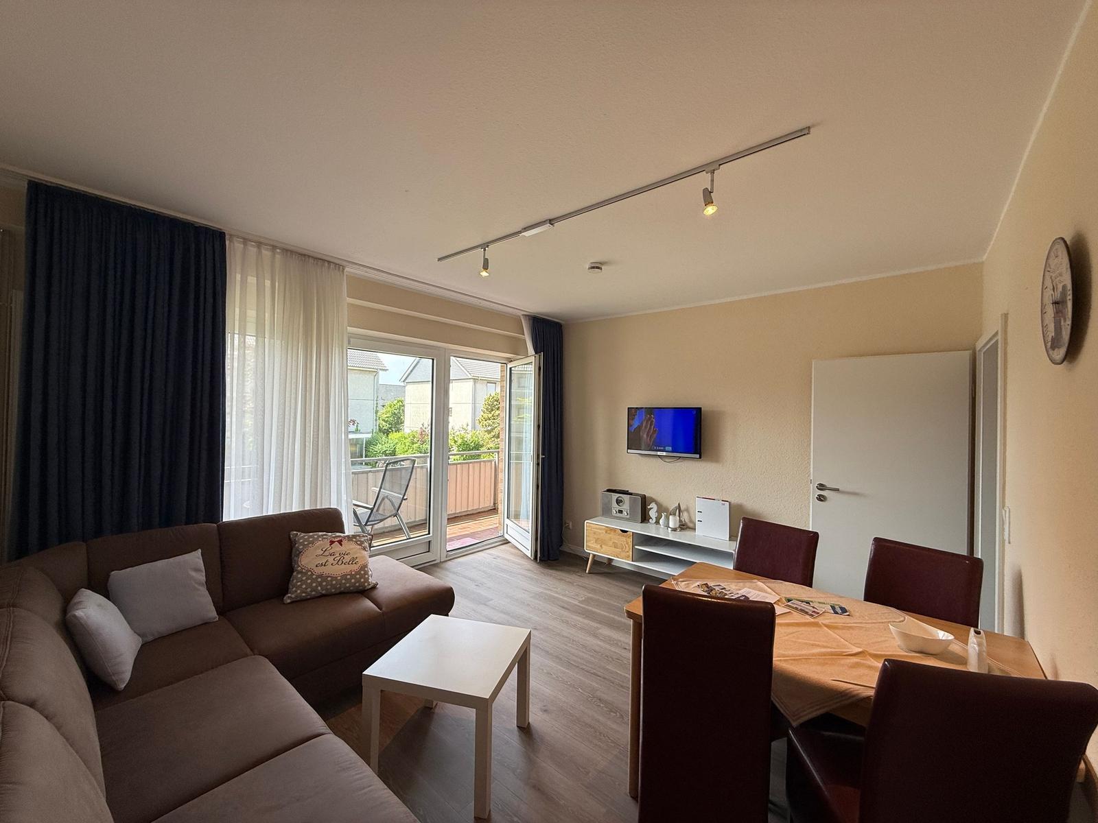 Wohn- und Essbereich mit Sofa, TV und Balkonzugang.