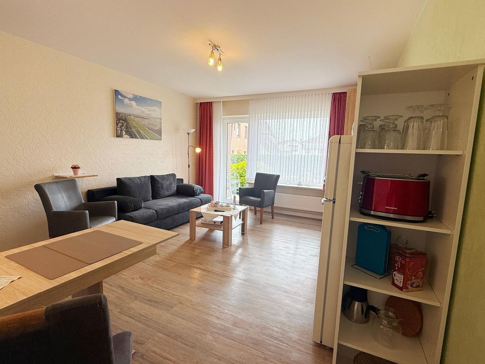Wohnzimmer mit Sofa, Esstisch und Küchenzeile mit Kühlschrank und Toaster.