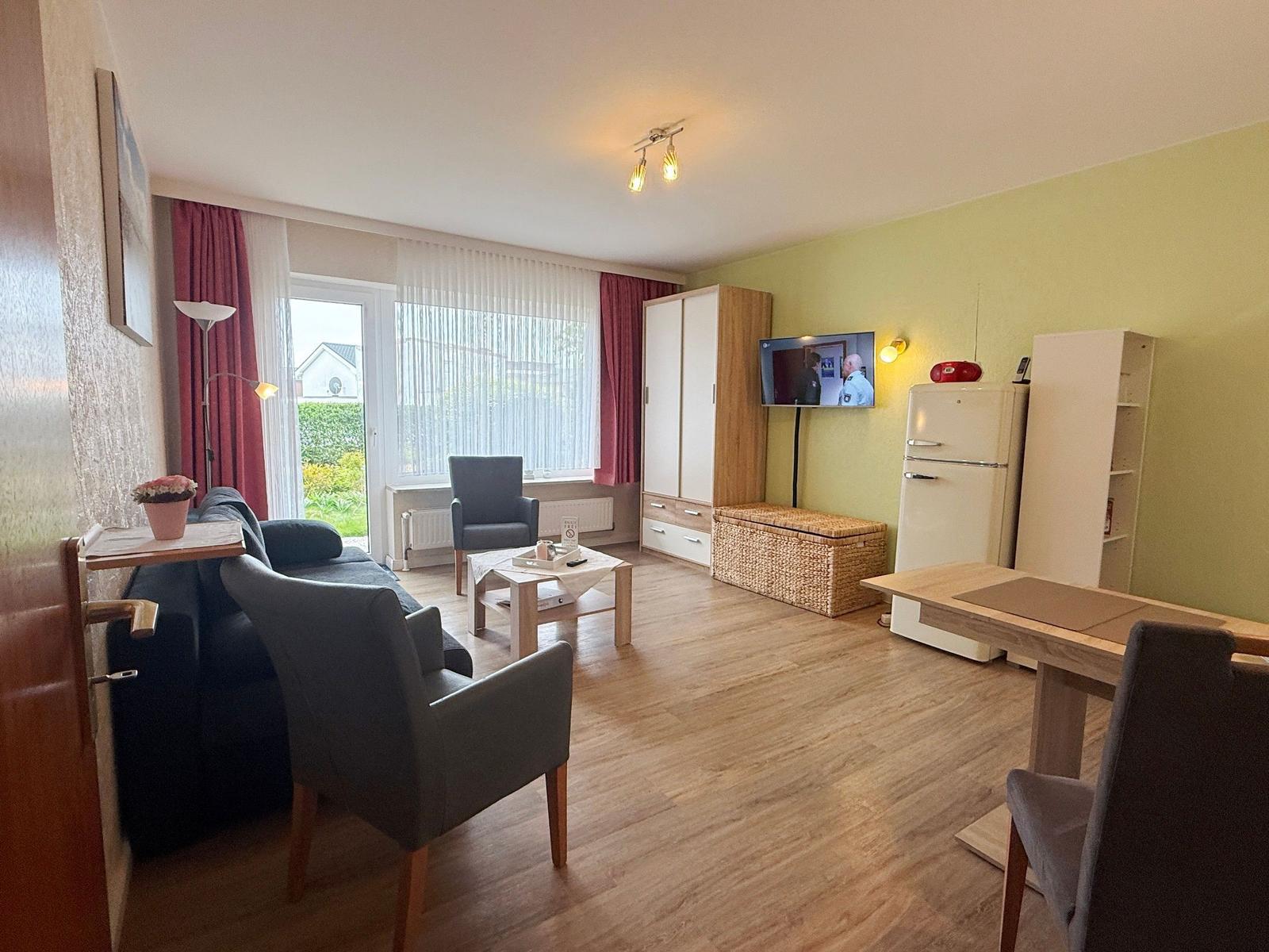 Wohnraum mit Sofa, Stühlen, Fernseher, Kühlschrank und Essbereich.