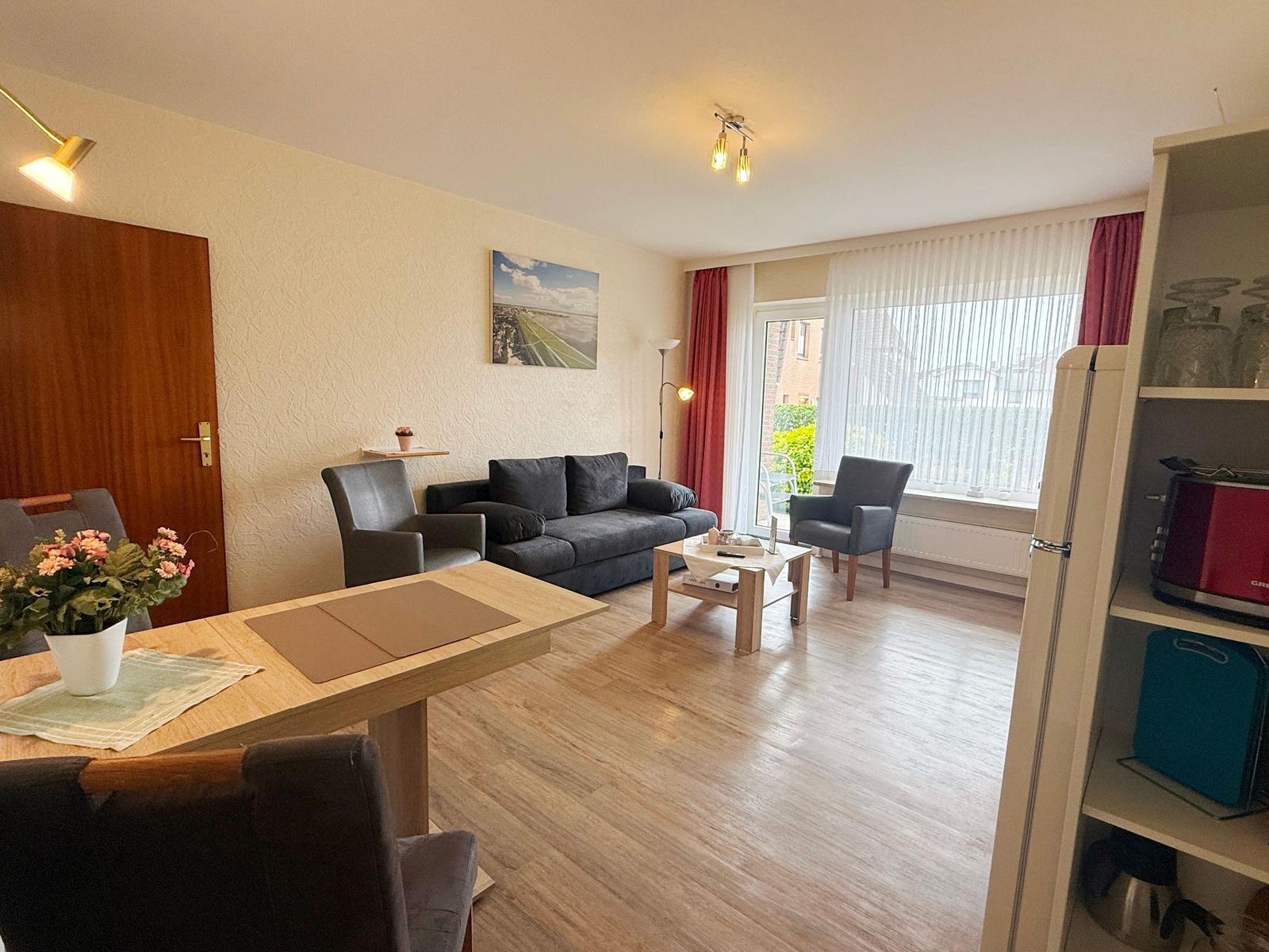 Wohnzimmer mit Sofa, Tisch und Fenster. Küchenzeile mit Schrank und Gerät.