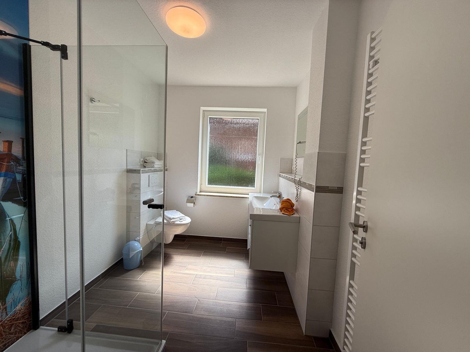 Badezimmer mit Dusche, Toilette, Waschbecken und Fenster.