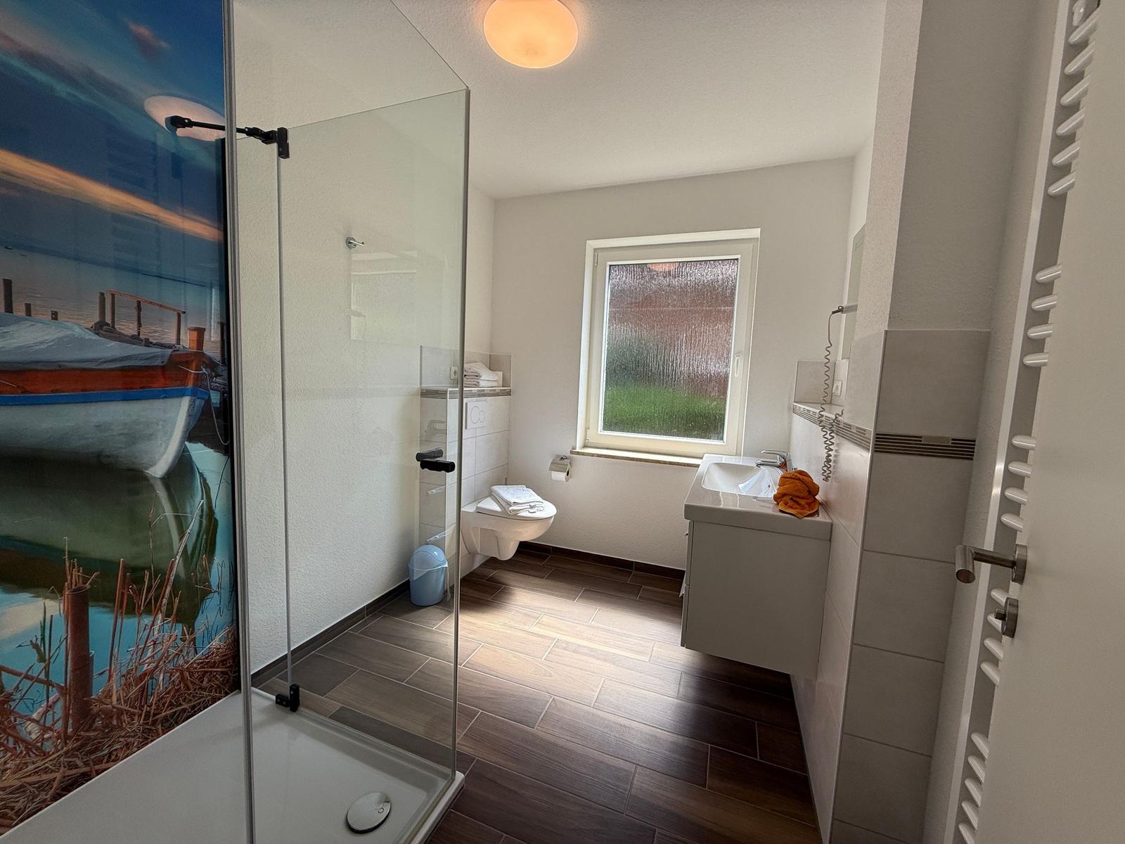 Badezimmer mit Dusche, Toilette und Waschbecken. Fenster mit grünem Blick.