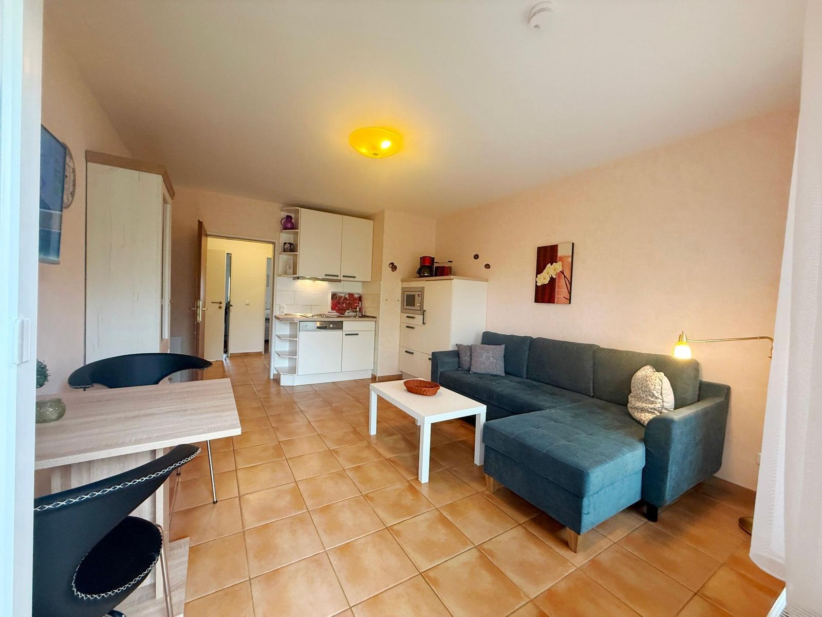 Wohnküche mit Sofa, Esstisch und Küchenschränken. Fliesenboden und Wandbild.