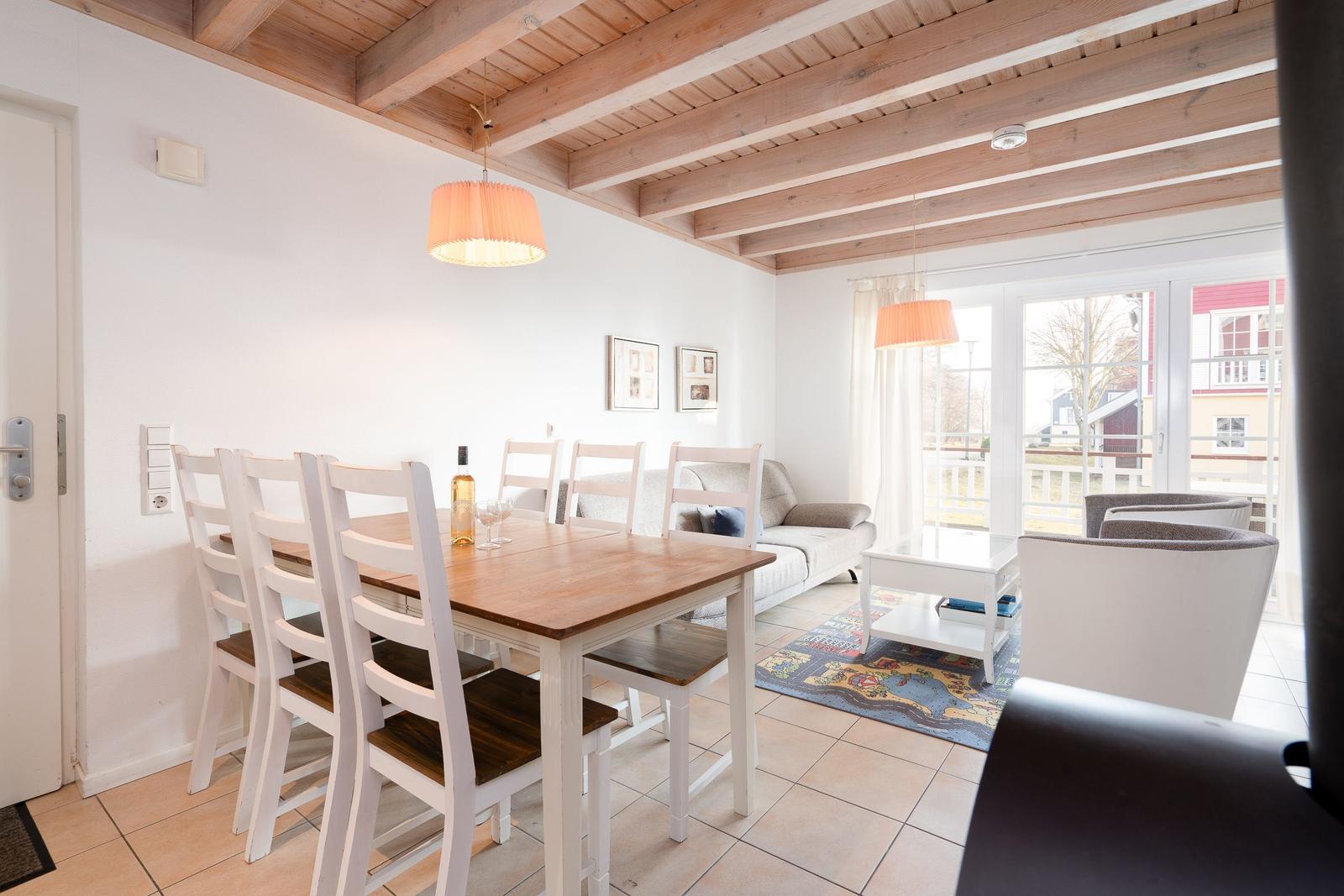 Dining area with table and chairs, living area with sofa and armchairs, wooden beam ceiling, large windows.