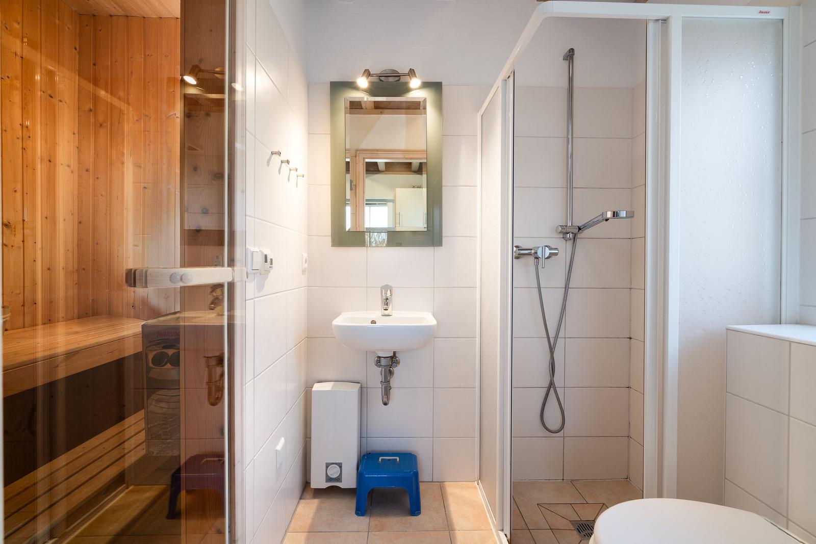 Bathroom with shower, sink, and sauna. Wooden frame and white tiles.